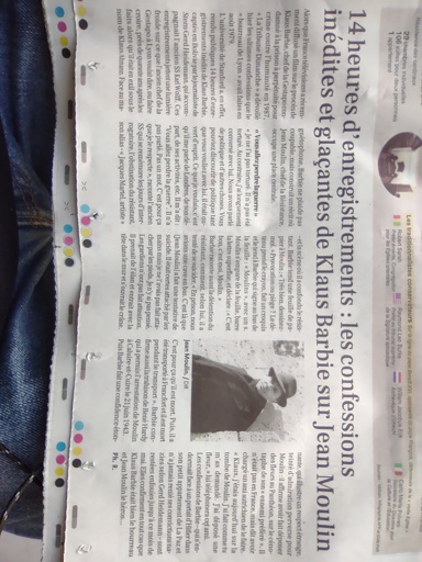 Une image prise au smartphone d'un article qui occupe le tiers bas d'un journal en papier. Le titre: "14 heures d'enregistrements : les confessions inedites et glacantes de Klaus Barbie sur Jean Moulin". L'article est aussi accompagné d'un portrait photo de Jean Moulin en noir et blanc, présumément avant sa mort dans les années 1930 ou 40.